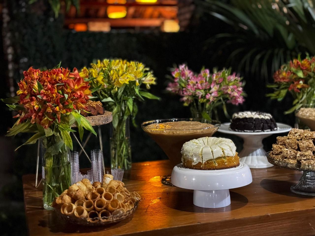 Mesa com bolos, doces caseiros e flores em um evento à noite