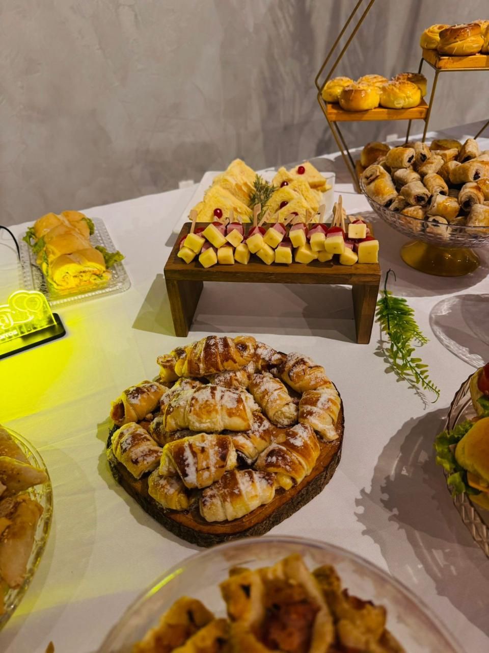 Mesa de coffee break com croissants, sanduíches e espetinhos de queijo em evento corporativo