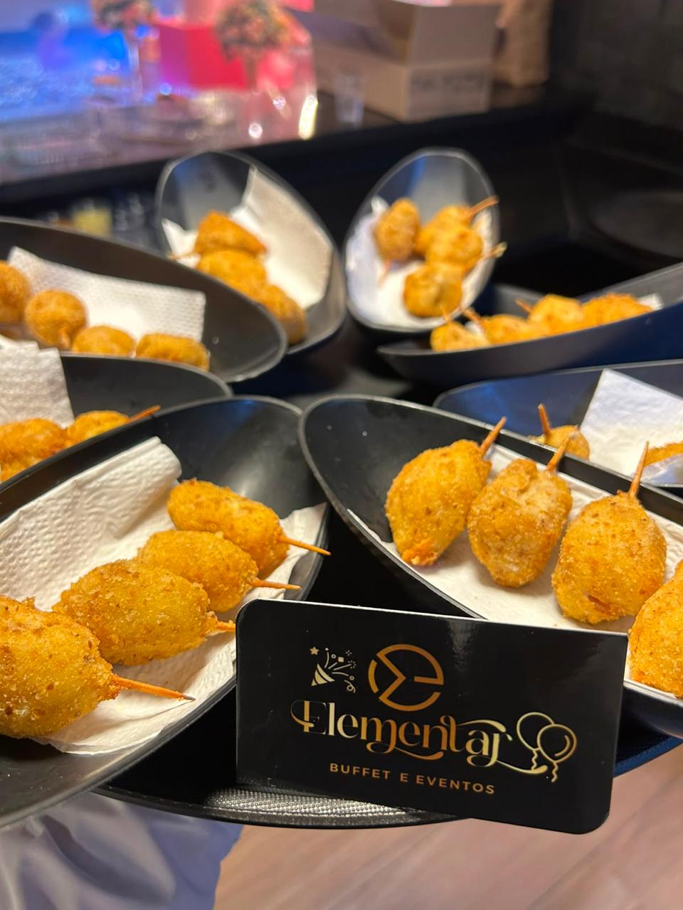 Bolinhos fritos no espeto servidos em travessas com o cartão da Elementar